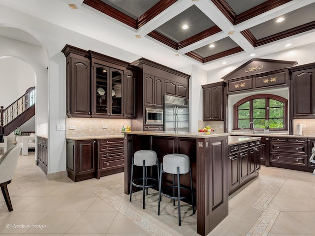 11315 77th St, Burr Ridge, IL 60527 - kitchen with built in appliances, a kitchen breakfast bar, dark brown cabinetry, a center island, and beam ceiling