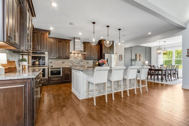 7166 Clubhouse Dr, Yorkville, IL 60560 - kitchen with wall chimney range hood, appliances with stainless steel finishes, a kitchen bar, dark brown cabinets, and backsplash