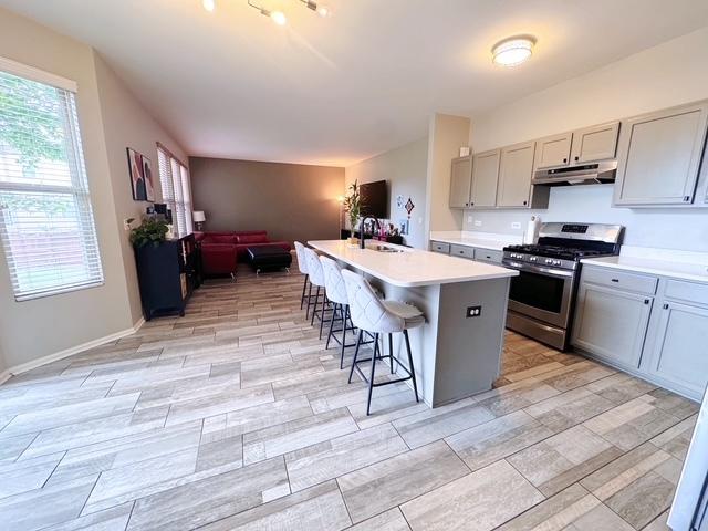 11319 Maplewood Dr, Plainfield, IL 60585 - kitchen with stainless steel gas range oven, under cabinet range hood, a sink, gray cabinets, and a kitchen breakfast bar