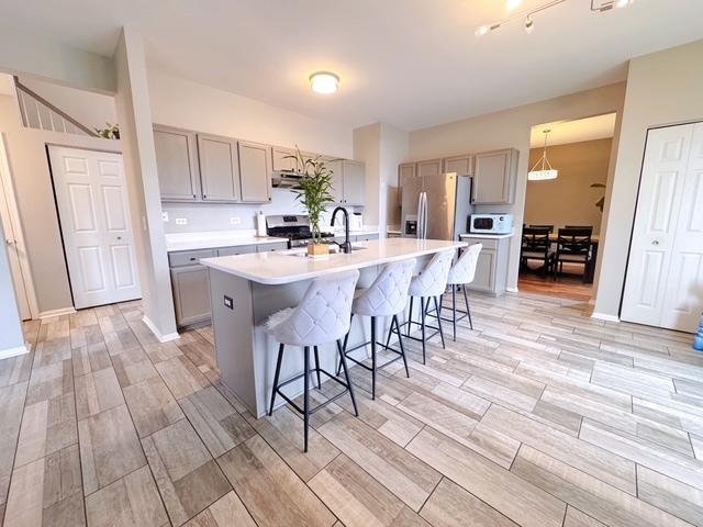 11319 Maplewood Dr, Plainfield, IL 60585 - kitchen with stainless steel appliances, gray cabinets, a sink, a breakfast bar area, and light countertops
