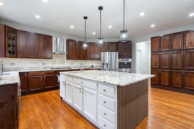 24723 W Champion Dr, Plainfield, IL 60585 - kitchen featuring stainless steel appliances, wall chimney exhaust hood, light wood-style flooring, a kitchen island with sink, and white cabinetry