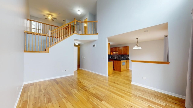 16158 Hillcrest Cir, Orland Park, IL 60467 - unfurnished living room featuring ceiling fan, light wood-style floors, stairway, a towering ceiling, and a chandelier