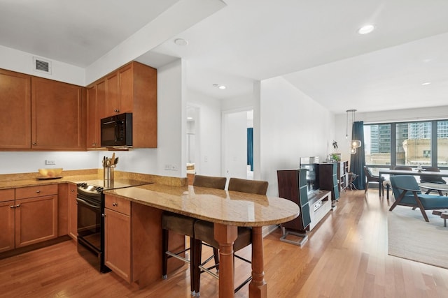 130 N Garland Ct Unit 2406, Chicago, IL 60602 - kitchen with black appliances, a breakfast bar, a peninsula, light wood-style floors, and light stone counters