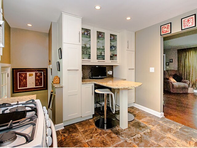 1424 Jerele Ave, Berkeley, IL 60163 - kitchen featuring white cabinetry, light stone counters, glass insert cabinets, a breakfast bar area, and recessed lighting