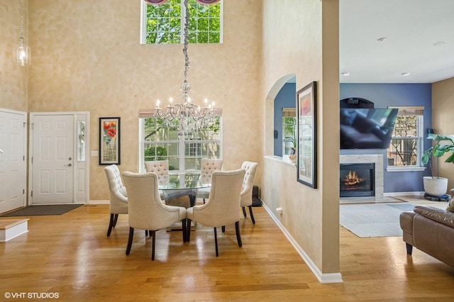 6068 Halloran Ln, Hoffman Estates, IL 60192 - dining area featuring light wood finished floors, a chandelier, a glass covered fireplace, baseboards, and a high ceiling