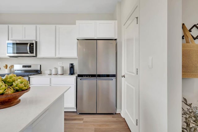 kitchen with appliances with stainless steel finishes, light countertops, light wood-type flooring, and white cabinets
