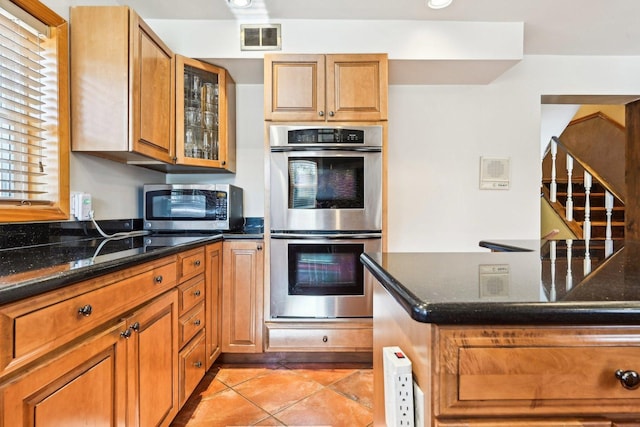 8252 N Caldwell Ave, Niles, IL 60714 - kitchen with appliances with stainless steel finishes, dark stone counters, light tile patterned flooring, glass insert cabinets, and brown cabinets