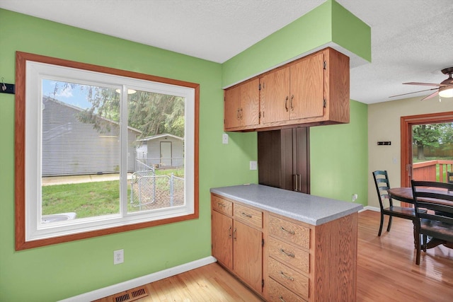 907 S Trailside Dr, Mahomet, IL 61853 - kitchen featuring a peninsula, light wood-style flooring, a textured ceiling, light countertops, and a ceiling fan