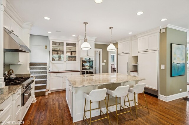 548 Cherry St, Winnetka, IL 60093 - kitchen featuring under cabinet range hood, dark wood finished floors, white cabinets, an island with sink, and stainless steel double oven