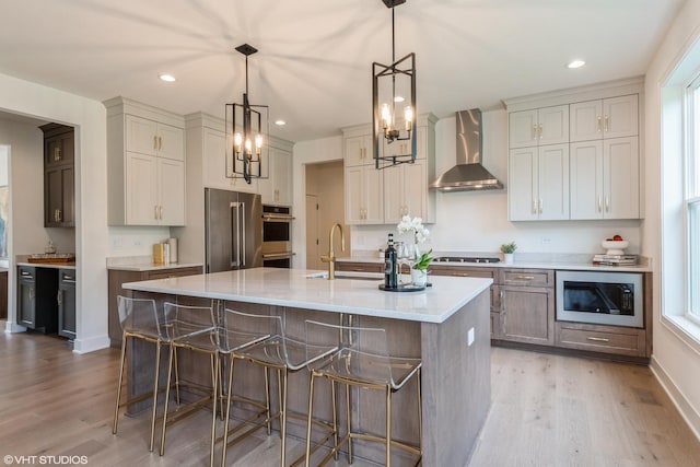 6030 Fairview Ave, Downers Grove, IL 60516 - kitchen with wall chimney exhaust hood, stainless steel appliances, light wood-type flooring, a breakfast bar, and an island with sink