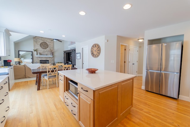 13119 Millbank Dr, Plainfield, IL 60585 - kitchen with stainless steel appliances, a fireplace, light wood-style flooring, light countertops, and a kitchen island