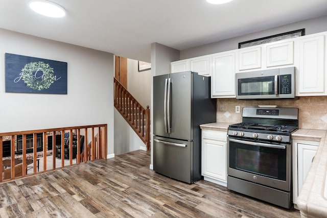 7812 Rhonda Dr, Roscoe, IL 61073 - kitchen featuring appliances with stainless steel finishes, white cabinetry, wood finished floors, decorative backsplash, and tile counters