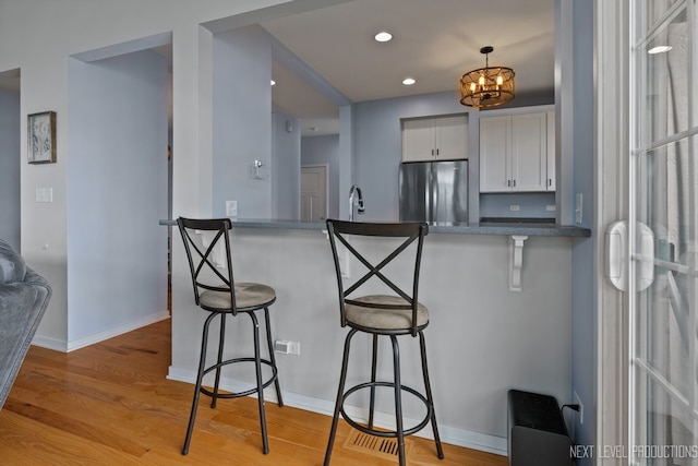 12709 Wild Rye Ct, Plainfield, IL 60585 - kitchen featuring freestanding refrigerator, a breakfast bar area, light wood-style floors, white cabinets, and a chandelier