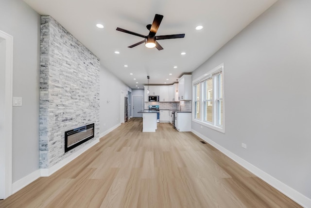 5731 S Damen Ave, Chicago, IL 60636 - unfurnished living room with a ceiling fan, light wood finished floors, a stone fireplace, recessed lighting, and baseboards