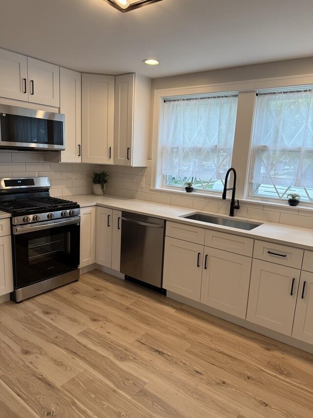 5301 S Mcvicker Ave, Chicago, IL 60638 - kitchen featuring appliances with stainless steel finishes, a sink, white cabinetry, light wood-type flooring, and healthy amount of natural light