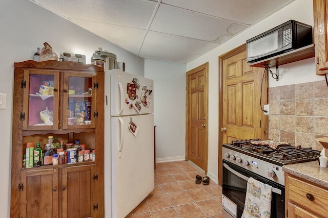 3342 S Aberdeen St, Chicago, IL 60608 - kitchen with stainless steel gas range oven, black microwave, freestanding refrigerator, light tile patterned floors, and a paneled ceiling
