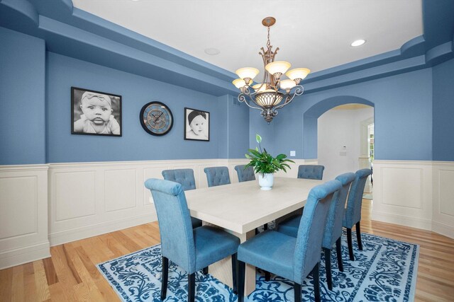 24355 S Arranmore Way, Frankfort, IL 60423 - dining space with arched walkways, light wood-style floors, a chandelier, a raised ceiling, and a wainscoted wall