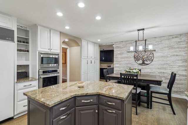 7316 Gleneagle Cir, Lakewood, IL 60014 - kitchen featuring built in appliances, arched walkways, white cabinets, wood finished floors, and light stone countertops