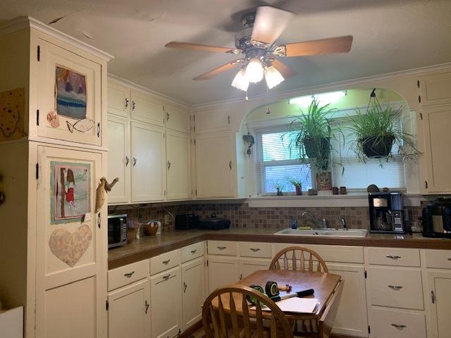 1013 Guion St, Ottawa, IL 61350 - kitchen featuring a sink, ceiling fan, decorative backsplash, white cabinetry, and crown molding