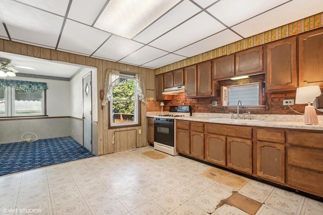2630 N Austin Ave, Chicago, IL 60639 - kitchen with white gas range oven, a sink, under cabinet range hood, wooden walls, and brown cabinets