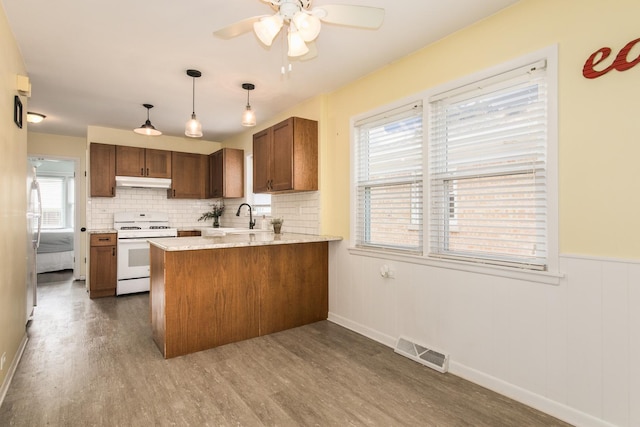 6136 N Nagle Ave, Chicago, IL 60646 - kitchen featuring white range with gas cooktop, under cabinet range hood, a peninsula, wood finished floors, and ceiling fan