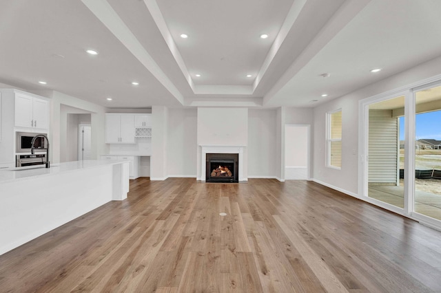 3245 Lincoln Prairie Blvd, Aurora, IL 60503 - unfurnished living room with recessed lighting, light wood-style floors, a fireplace with flush hearth, baseboards, and a tray ceiling