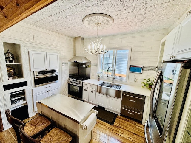 3515 Union Ave, Steger, IL 60475 - kitchen featuring stainless steel appliances, wall chimney exhaust hood, a sink, light wood-style flooring, and a chandelier