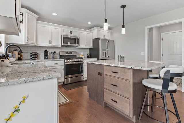 1607 Peppermill Ln, Champaign, IL 61822 - kitchen with appliances with stainless steel finishes, a breakfast bar, decorative backsplash, dark wood finished floors, and a center island