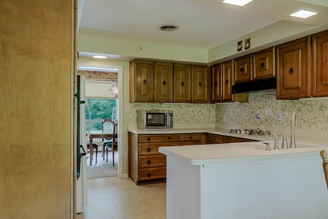 kitchen featuring under cabinet range hood, stainless steel microwave, a peninsula, light countertops, and a sink