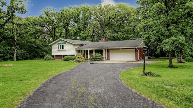 tri-level home with an attached garage, brick siding, driveway, a front yard, and a chimney