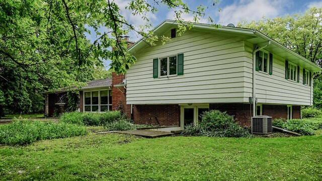 view of home's exterior with a chimney, a yard, central air condition unit, and brick siding