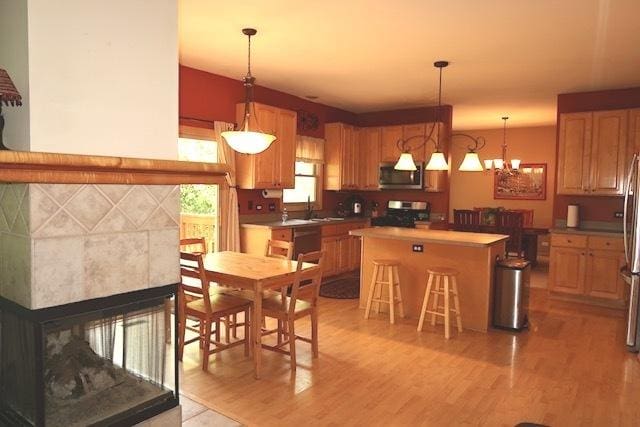 957 Chancery Ln, Cary, IL 60013 - kitchen with appliances with stainless steel finishes, a kitchen island, light wood-style flooring, a sink, and a tile fireplace