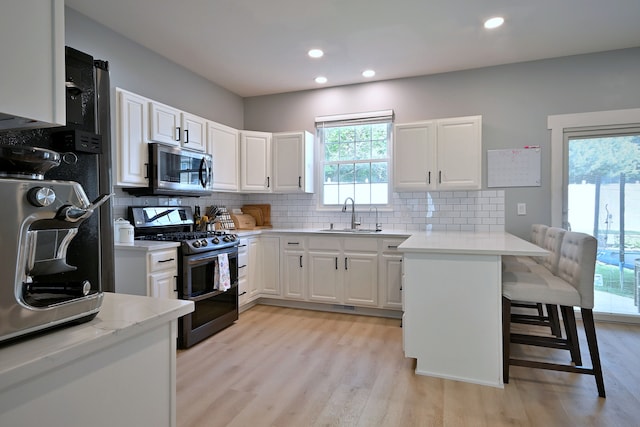 1422 Deer Creek Ln, Lake In The Hills, IL 60156 - kitchen featuring appliances with stainless steel finishes, a sink, a peninsula, a kitchen bar, and light wood-style flooring