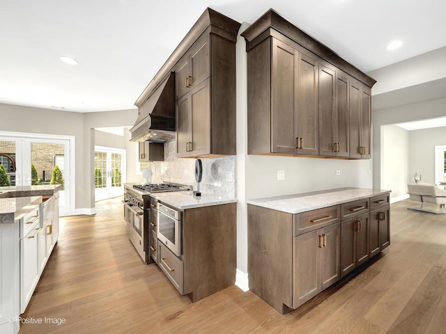 608 W 55th St, Hinsdale, IL 60521 - kitchen featuring appliances with stainless steel finishes, extractor fan, light wood-style flooring, tasteful backsplash, and light stone counters