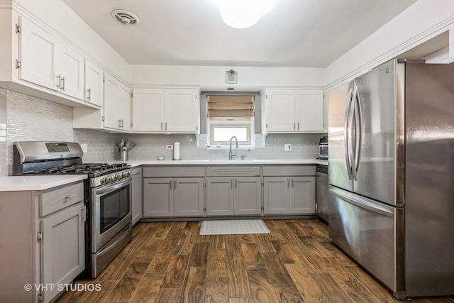 kitchen with appliances with stainless steel finishes, gray cabinetry, light countertops, dark wood-style floors, and decorative backsplash