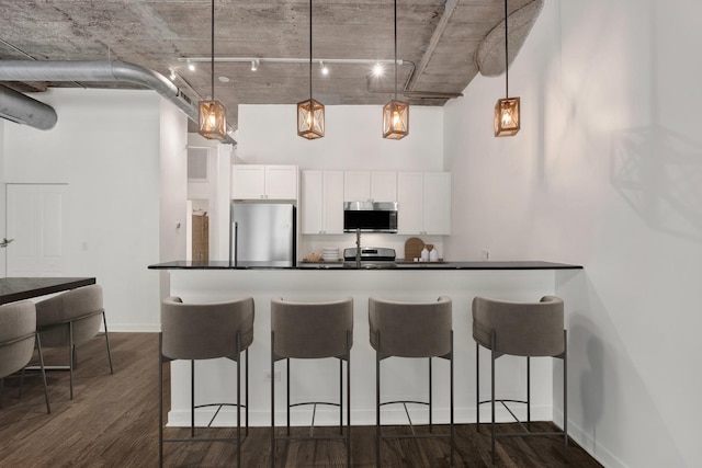 1110 W 15th St Unit 114, Chicago, IL 60608 - kitchen featuring appliances with stainless steel finishes, a towering ceiling, dark countertops, a kitchen breakfast bar, and white cabinets