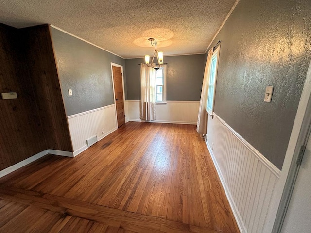 826 N 11th St, Rochelle, IL 61068 - empty room featuring wood finished floors, a wainscoted wall, a chandelier, ornamental molding, and a textured ceiling