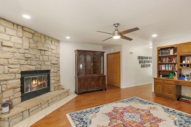 living room with a ceiling fan, a stone fireplace, wood finished floors, baseboards, and recessed lighting