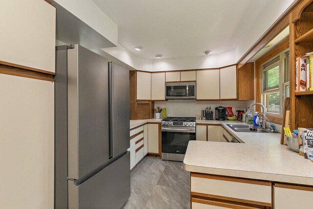 kitchen with appliances with stainless steel finishes, a sink, light countertops, and cream cabinets