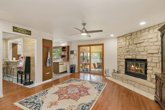 living area with a stone fireplace, ceiling fan, wood finished floors, and recessed lighting