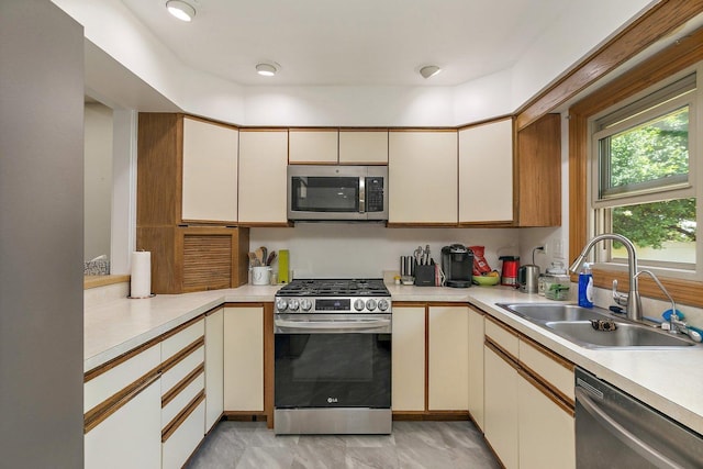 kitchen featuring stainless steel appliances, a sink, light countertops, and cream cabinetry