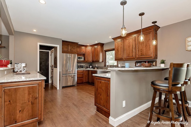 34942 N Gogol Ave, Ingleside, IL 60041 - kitchen featuring stainless steel appliances, a peninsula, brown cabinetry, wood finished floors, and hanging light fixtures