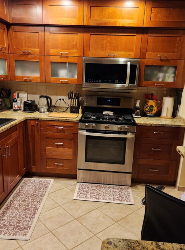 3300 N Carriageway Dr Unit 209, Arlington Heights, IL 60004 - kitchen with stainless steel appliances, light tile patterned floors, light stone countertops, glass insert cabinets, and brown cabinets
