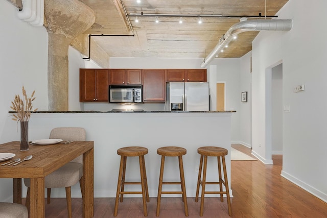 1111 W 14th Pl Unit 211, Chicago, IL 60608 - kitchen featuring stainless steel appliances, rail lighting, a breakfast bar, wood finished floors, and dark countertops