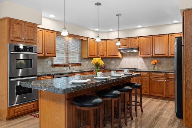 1291 Acorn Ct, Sleepy Hollow, IL 60118 - kitchen featuring stainless steel appliances, under cabinet range hood, brown cabinetry, light wood-style flooring, and a kitchen bar