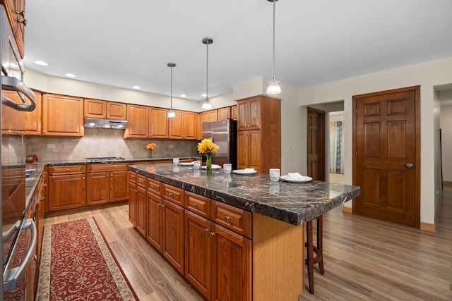 1291 Acorn Ct, Sleepy Hollow, IL 60118 - kitchen with appliances with stainless steel finishes, a breakfast bar area, under cabinet range hood, brown cabinets, and a kitchen island