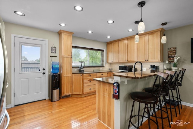 712 Cascade Ave, Romeoville, IL 60446 - kitchen with a peninsula, light wood-style flooring, light brown cabinetry, decorative backsplash, and a kitchen breakfast bar