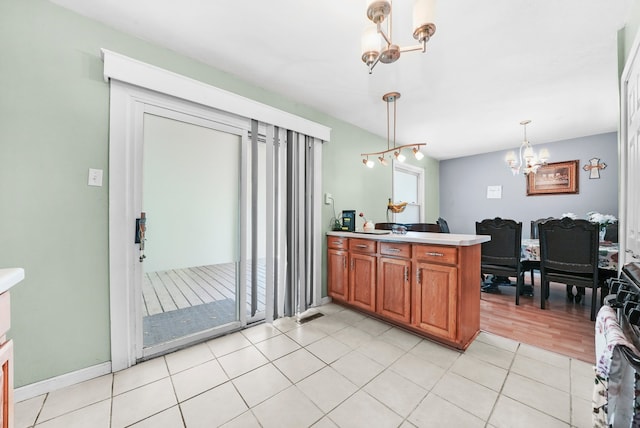 136 Anita Dr, Bourbonnais, IL 60914 - kitchen with a chandelier, brown cabinets, a peninsula, light tile patterned floors, and pendant lighting