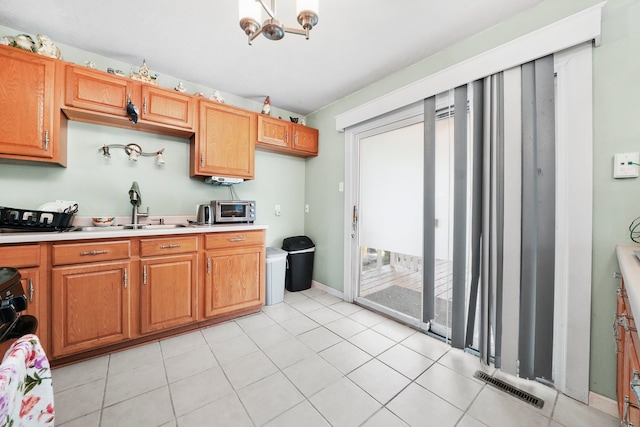 136 Anita Dr, Bourbonnais, IL 60914 - kitchen featuring light countertops, a sink, a chandelier, brown cabinetry, and light tile patterned floors
