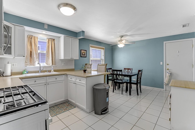4730 N Hermitage Ave Unit 2F, Chicago, IL 60640 - kitchen featuring ceiling fan, gas range, a peninsula, white cabinets, and tasteful backsplash